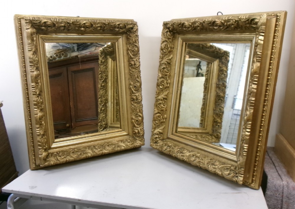 A pair of rectangular giltwood wall mirrors featuring heavily carved frame borders with acanthus leaf scrolling and beaded inner moulding.