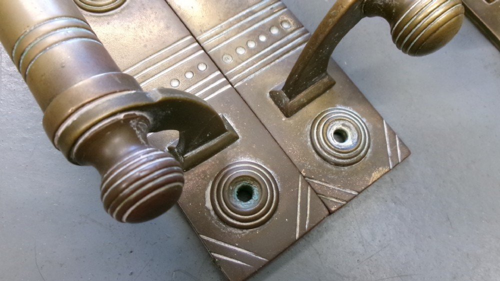Two pairs of Arts and Crafts brass pull door handles featuring rectangular backplates with incised geometric line detailing and turned cylindrical bar grips with spherical finials. View II