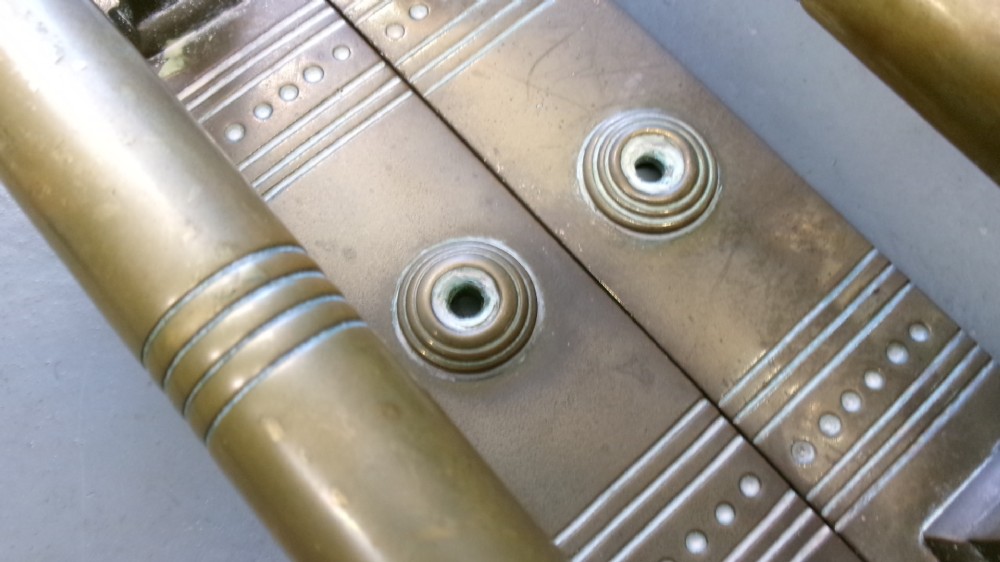 Two pairs of Arts and Crafts brass pull door handles featuring rectangular backplates with incised geometric line detailing and turned cylindrical bar grips with spherical finials. View III