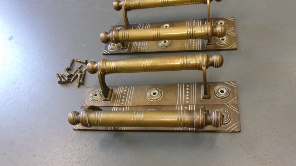 Two pairs of Arts and Crafts brass pull door handles featuring rectangular backplates with incised geometric line detailing and turned cylindrical bar grips with spherical finials. View IV