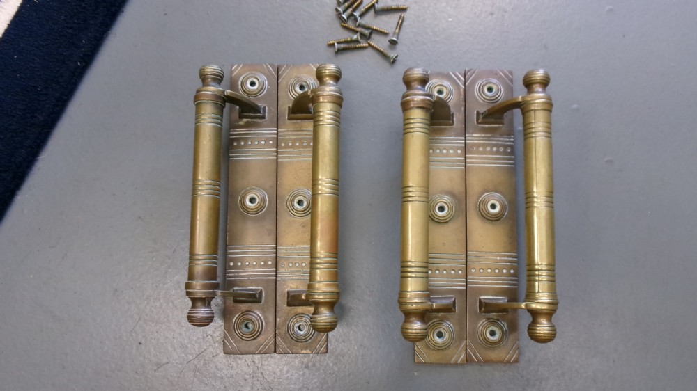 Two pairs of Arts and Crafts brass pull door handles featuring rectangular backplates with incised geometric line detailing and turned cylindrical bar grips with spherical finials. View VI