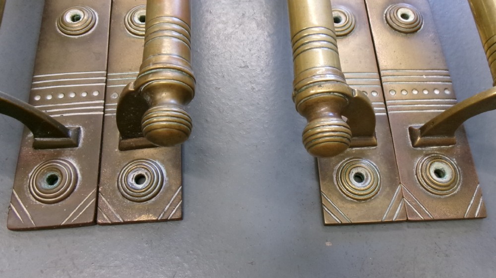 Two pairs of Arts and Crafts brass pull door handles featuring rectangular backplates with incised geometric line detailing and turned cylindrical bar grips with spherical finials. View XI