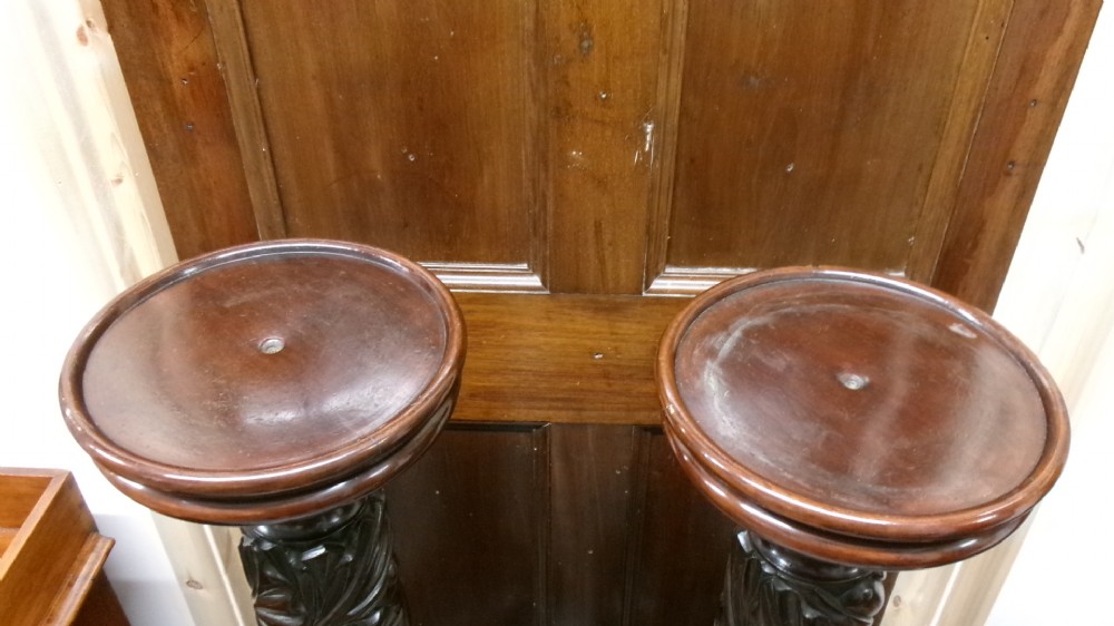 A pair of tall Victorian dark mahogany torchere stands featuring circular dished tops, spiral acanthus leaf carved shafts, and square plinth bases. View V