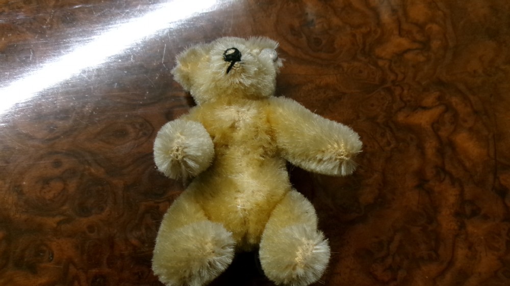A miniature honey-gold mohair teddy bear sitting down with hand-stitched facial details and a metal button in its left ear. View III