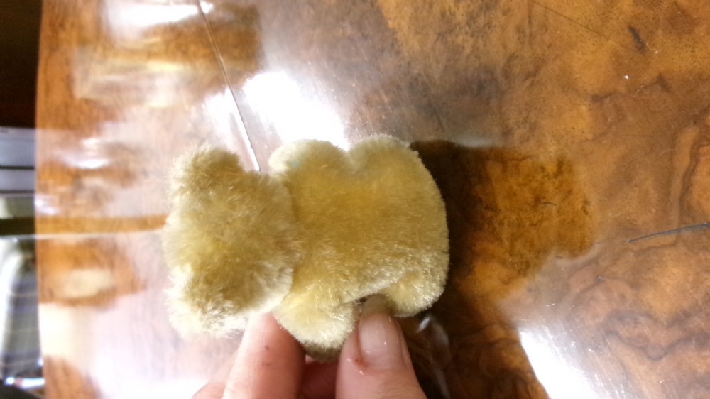 A miniature honey-gold mohair teddy bear sitting down with hand-stitched facial details and a metal button in its left ear. View IV