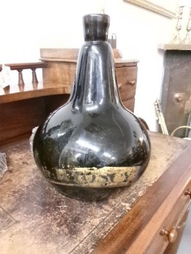 A large dark green hand-blown Georgian glass onion bottle with a bulbous body, narrow neck, and a faded gilt label near the base.