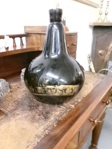 A large dark green hand-blown Georgian glass onion bottle with a bulbous body, narrow neck, and a faded gilt label near the base. View III
