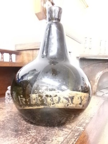 A large dark green hand-blown Georgian glass onion bottle with a bulbous body, narrow neck, and a faded gilt label near the base. View IV