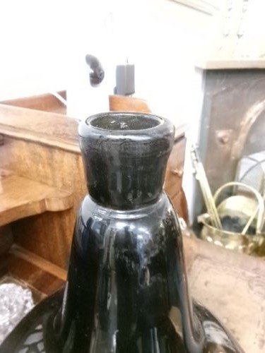 A large dark green hand-blown Georgian glass onion bottle with a bulbous body, narrow neck, and a faded gilt label near the base. View VI