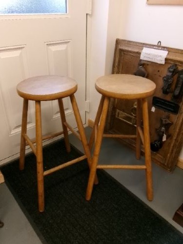 A pair of tall wooden bar stools featuring circular elm seats, splayed turned legs, and lower supporting stretchers.