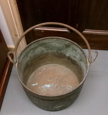 A Victorian metal cauldron featuring a deep circular body, a folded top rim, surface oxidisation, and an arched swing handle attached to side loops. View III