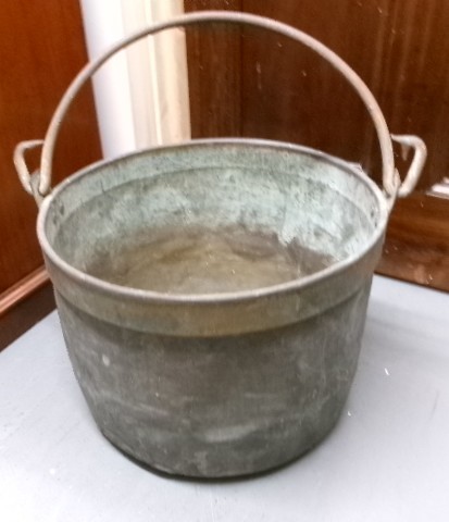 A Victorian metal cauldron featuring a deep circular body, a folded top rim, surface oxidisation, and an arched swing handle attached to side loops. View VIII