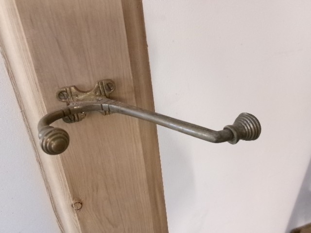A long vertical pine wood backboard fitted with four double-pronged brass coat hooks. View II