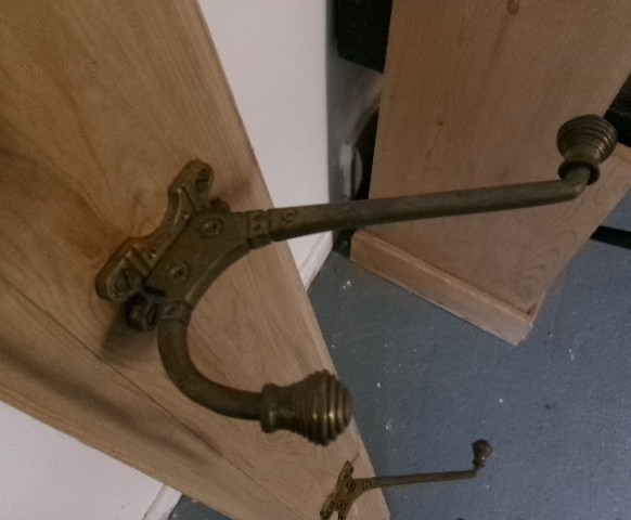 A long vertical pine wood backboard fitted with four double-pronged brass coat hooks. View III