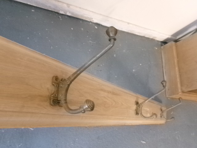 A long vertical pine wood backboard fitted with four double-pronged brass coat hooks. View IV