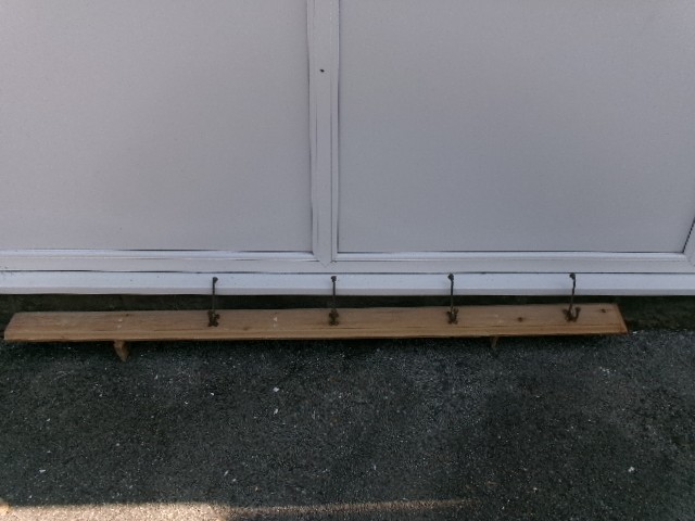 A long vertical pine wood backboard fitted with four double-pronged brass coat hooks. View VI