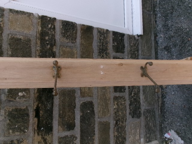 A long vertical pine wood backboard fitted with four double-pronged brass coat hooks. View IX