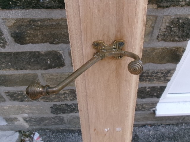 A long vertical pine wood backboard fitted with four double-pronged brass coat hooks. View X