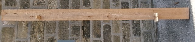 A long vertical pine wood backboard fitted with four double-pronged brass coat hooks. View XII