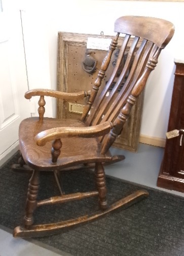 A Victorian dark oak rocking chair featuring a shaped crest rail, vertical spindles, turned arm supports, a solid wooden seat, and curved runners. View II