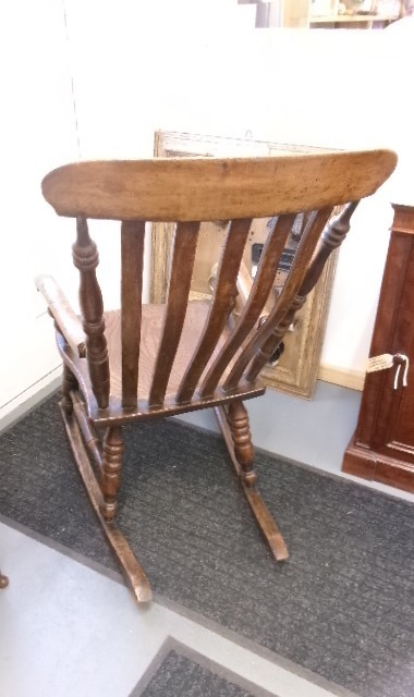 A Victorian dark oak rocking chair featuring a shaped crest rail, vertical spindles, turned arm supports, a solid wooden seat, and curved runners. View VII