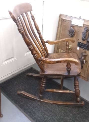 A Victorian dark oak rocking chair featuring a shaped crest rail, vertical spindles, turned arm supports, a solid wooden seat, and curved runners. View IX