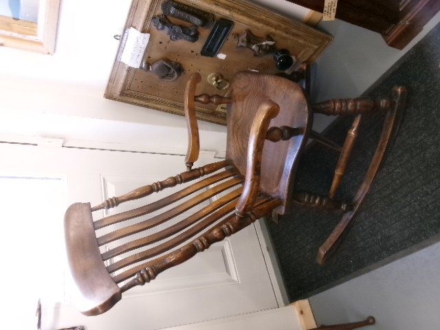 A Victorian dark oak rocking chair featuring a shaped crest rail, vertical spindles, turned arm supports, a solid wooden seat, and curved runners. View X