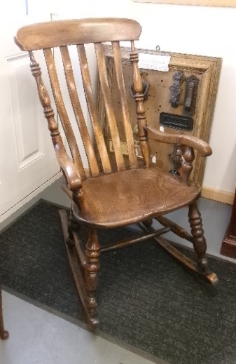 A Victorian dark oak rocking chair featuring a shaped crest rail, vertical spindles, turned arm supports, a solid wooden seat, and curved runners. View XI
