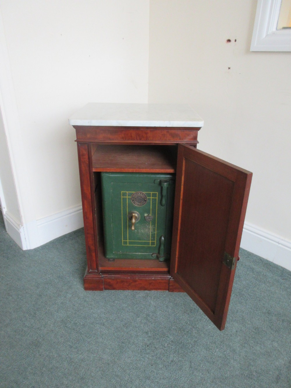 A Victorian mahogany cabinet with a white marble top, featuring an open door revealing an enclosed green cast iron safe inside.