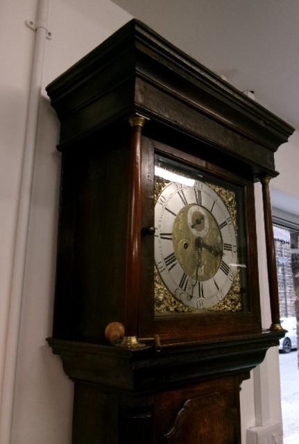 An 18th-century Georgian dark oak longcase clock featuring a square brass dial, fluted hood columns, and a moulded base. View VI