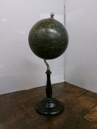 A 1930s celestial globe with a dark green sphere depicting printed constellations, supported on a turned ebonised black wooden stand with a metal axis. View IX