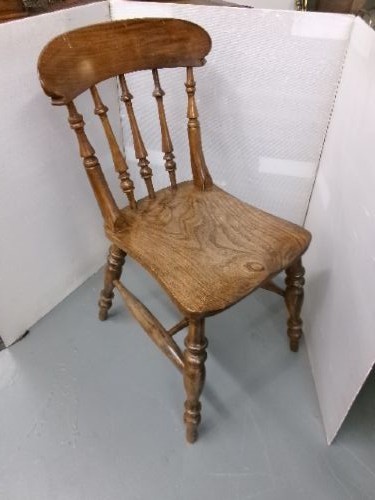 A Victorian wooden kitchen chair featuring a shaped elm seat, turned spindles, curved top crest rail, and turned legs with stretchers.