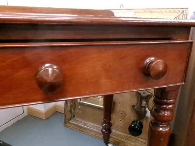 A nineteenth-century Victorian mahogany writing table featuring a low rear gallery, twin drawers with turned wooden knobs, and turned tapered legs resting on white ceramic castors. View III