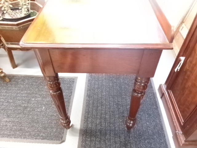 A nineteenth-century Victorian mahogany writing table featuring a low rear gallery, twin drawers with turned wooden knobs, and turned tapered legs resting on white ceramic castors. View VI