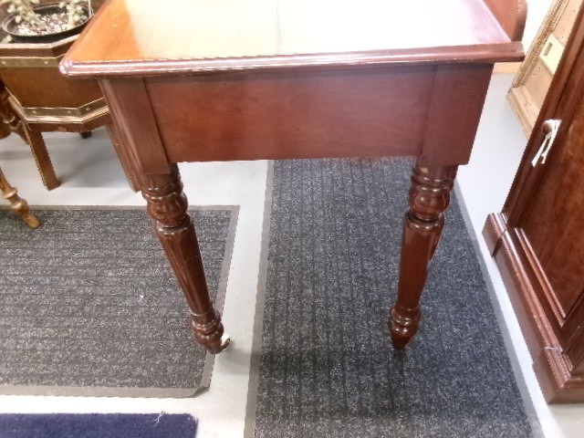 A nineteenth-century Victorian mahogany writing table featuring a low rear gallery, twin drawers with turned wooden knobs, and turned tapered legs resting on white ceramic castors. View VII
