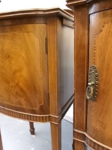 A pair of Edwardian mahogany bedside cabinets featuring bow fronts, satinwood string inlay, shaped upstands, and tapered legs. View IX