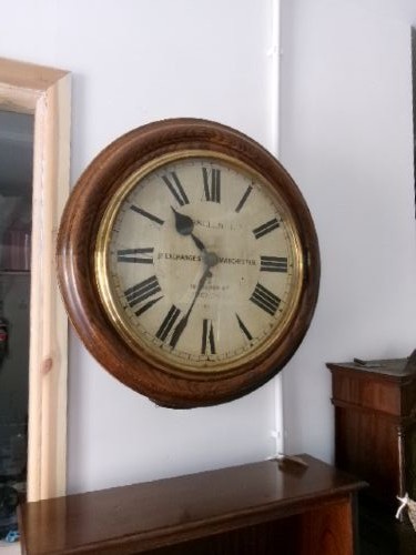 A circular antique wall clock housed in a thick moulded oak case with a glazed brass bezel and painted dial displaying Roman numerals. View X