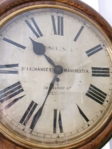 A circular antique wall clock housed in a thick moulded oak case with a glazed brass bezel and painted dial displaying Roman numerals. View IX