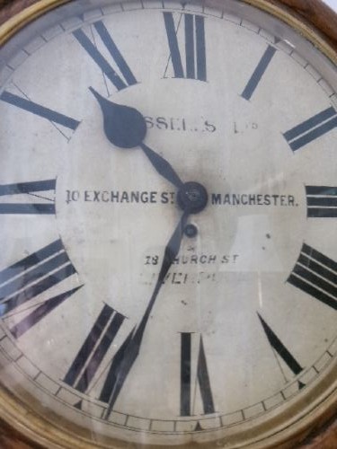 A circular antique wall clock housed in a thick moulded oak case with a glazed brass bezel and painted dial displaying Roman numerals. View VIII