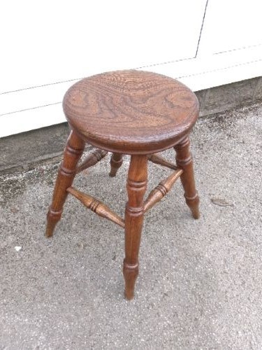 An antique Victorian wooden tavern stool featuring a circular thick elm seat and turned splayed legs joined by stretchers. View VII