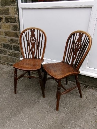 A pair of traditional wooden Windsor chairs featuring contoured elm seats, pierced wheelback splats, hoop backs, and turned legs connected by H-stretchers. View X