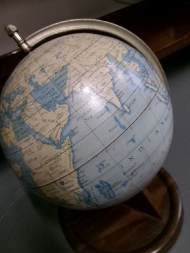 A vintage tinplate world globe with a pale blue lithographed ocean map mounted on a circular metal base with a curved semi-meridian arm. View II