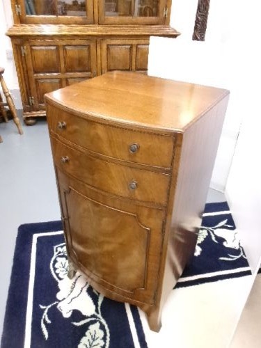 An Edwardian bow-front mahogany cabinet featuring two upper drawers with brass knobs over a panelled cupboard door. View IV