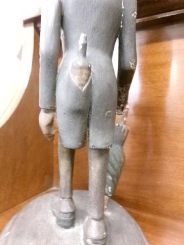 A carved and painted wooden figure of a caricatured man wearing a top hat and tailcoat, holding an umbrella while standing on a rounded grey base. View V