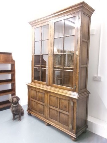 A large two-section warm brown oak bookcase featuring two upper glazed doors with internal shelves above two lower field-panelled wooden doors. View II
