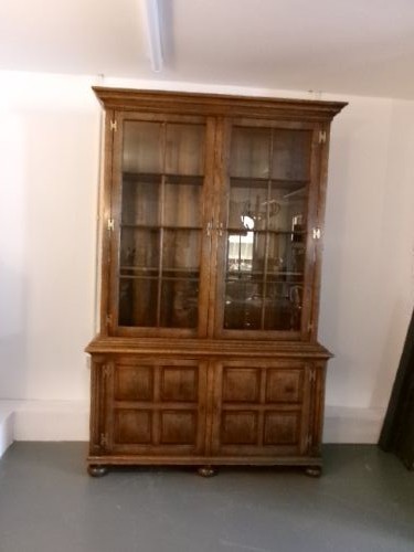 A large two-section warm brown oak bookcase featuring two upper glazed doors with internal shelves above two lower field-panelled wooden doors.