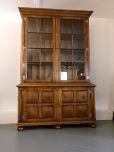 A large two-section warm brown oak bookcase featuring two upper glazed doors with internal shelves above two lower field-panelled wooden doors. View IV