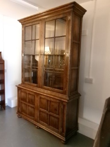 A large two-section warm brown oak bookcase featuring two upper glazed doors with internal shelves above two lower field-panelled wooden doors. View V