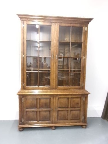 A large two-section warm brown oak bookcase featuring two upper glazed doors with internal shelves above two lower field-panelled wooden doors. View VI