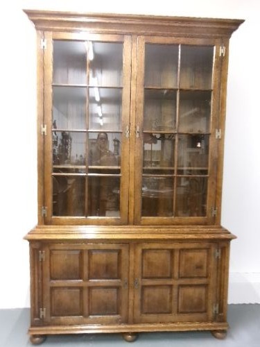 A large two-section warm brown oak bookcase featuring two upper glazed doors with internal shelves above two lower field-panelled wooden doors. View VII
